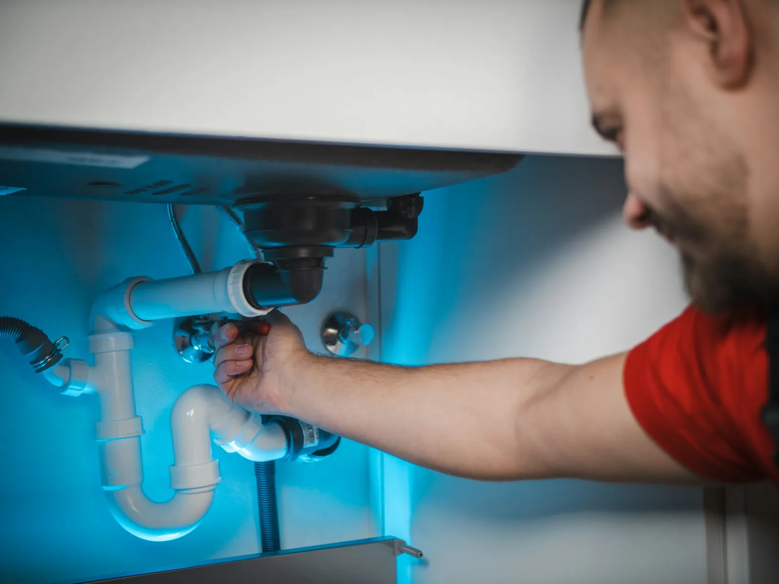 Smiling plumber fixing the drain pipes under a sink